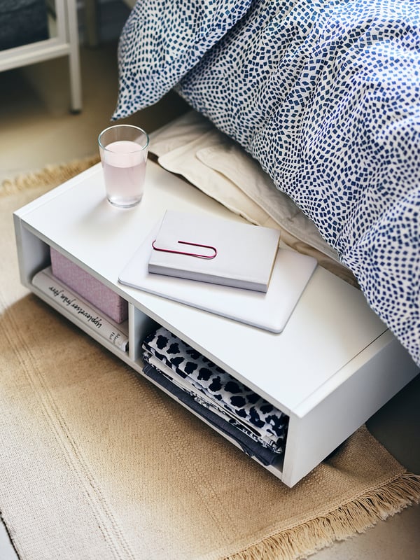 Bedside table with books, a glass, and a patterned bedspread.