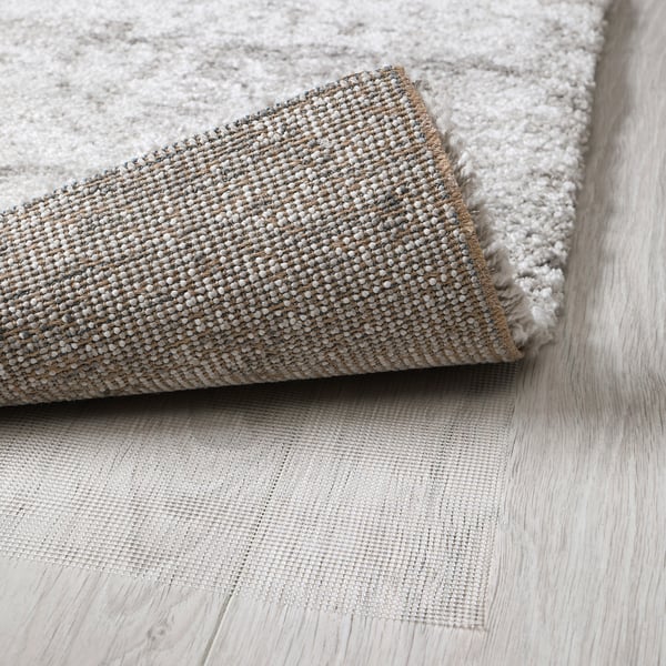 A rolled-up grey rug with thick, textured pile, laid on light wooden flooring. The dense weave suggests comfort and sound absorption.