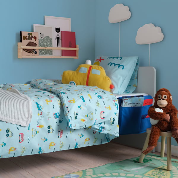 Childrens bedroom with blue walls, vehicle-patterned duvet, aeroplane pillow, bookshelf with cat art, monkey toy, book pocket.