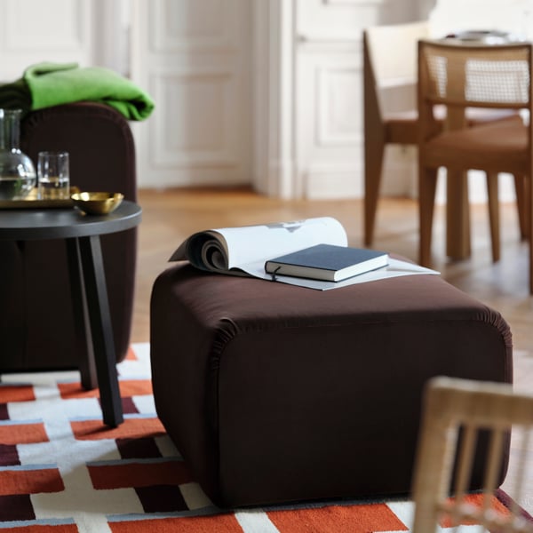 Brown stool with rug and book, colourful rug, side table with glassware in living area.