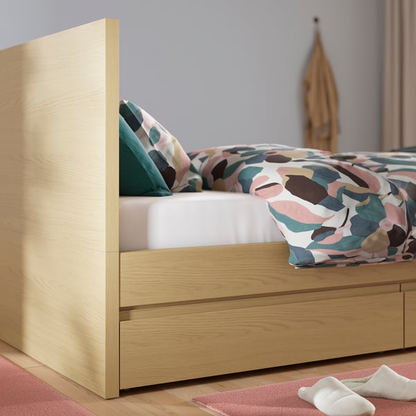 A modern wooden bed with storage drawers. Patterned bedding and pillows on a comfortable mattress.