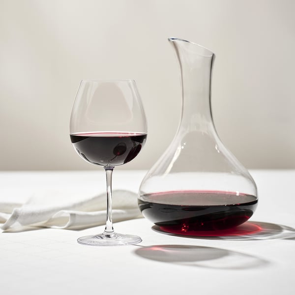 Transparent wine decanter and glass on white tablecloth, filled with red wine for tasting.