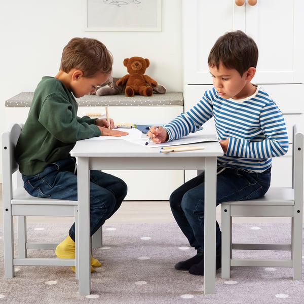 Two kids sitting at a small white table, drawing with crayons.