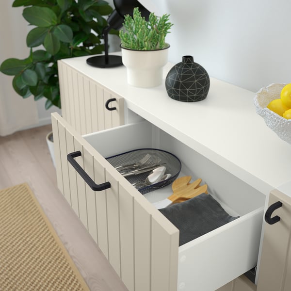Open drawer of white SUTTERVIKEN cabinet, showing black mesh cutlery tray with utensils and wooden spatulas.