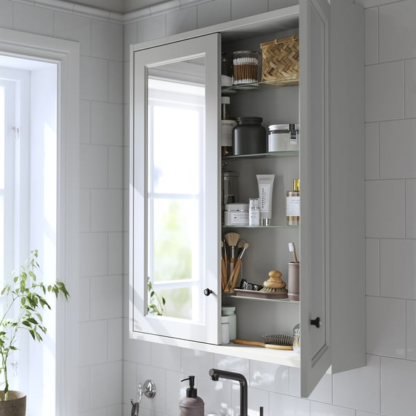 Open grey mirror cabinet displaying toiletries, mounted above white sink, set against tiled wall.