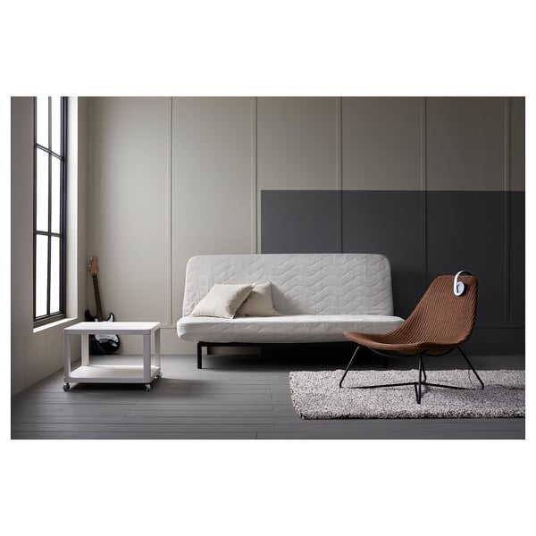 Modern minimalist living area with white futon, wicker chair, and white side table with castors.