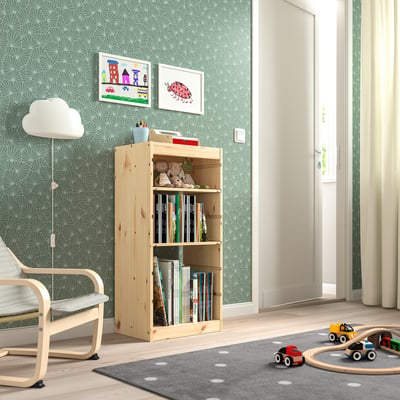 Childs room with TROFAST light wood storage shelf holding books and toys. Bright wallpaper, rug, and floor lamp. Toy cars and chair visible.