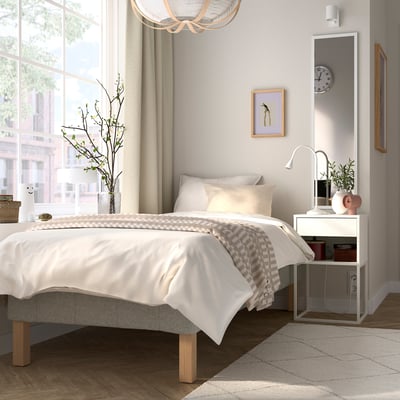 A cosy bedroom with a large bed, white bedding, and wooden bedside table. The floor has a neutral-colored rug, slightly smaller than the bed.
