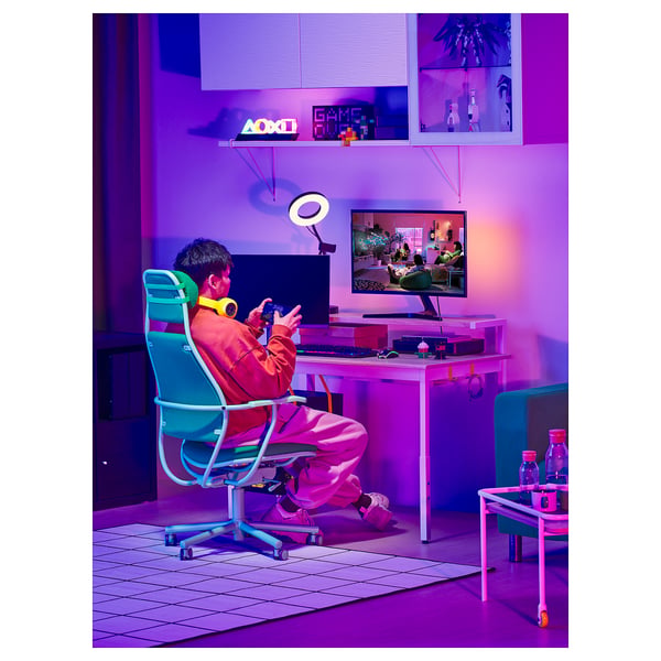 Gamer sits at customizable UTVISNING desk with neon lights, playing video games.