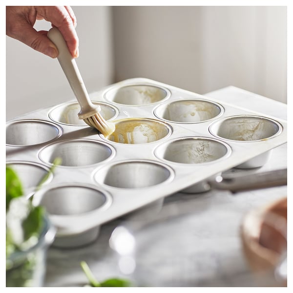 Person greasing VARDAGEN muffin tin, silver, with brush, preparing to bake.