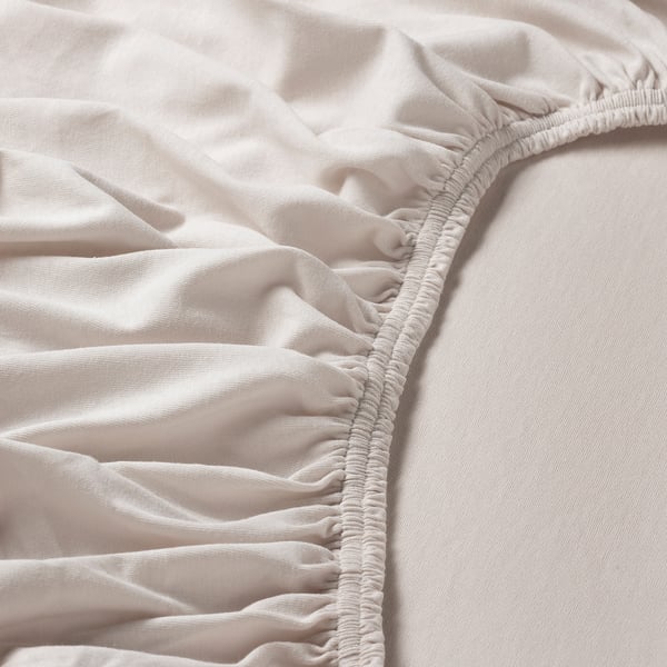 Close-up of soft, creased white fabric with fine stitching, likely a bed sheet, showcasing its smooth texture and quality material.