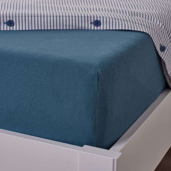 Blue cotton sheet on white bed, showing fitted corners.