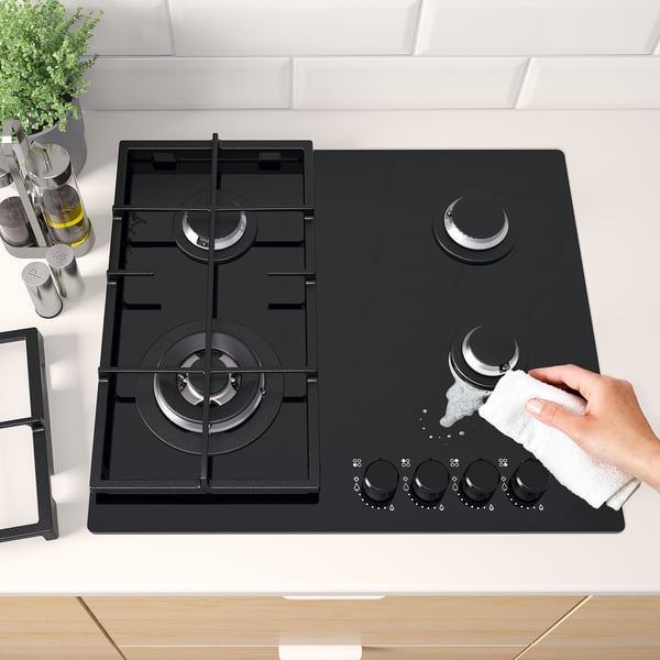 Hand cleaning black gas hob with four burners and electronic ignition knobs.
