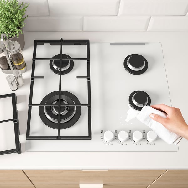 Person cleaning a gas hob with cast iron supports and control knobs on the front.