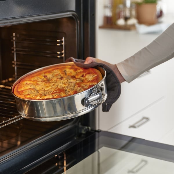 Removing pizza from oven with springform tin for even heat and easy serving.