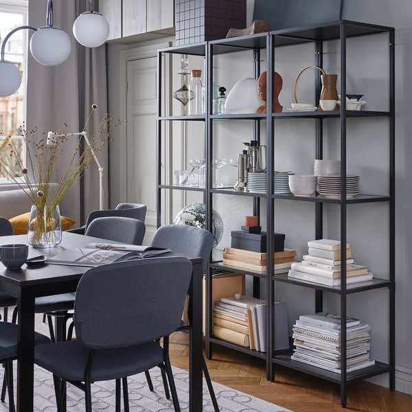 Modern dining set with chairs, black bookshelves, decor, window.