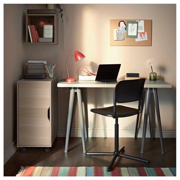 Kaasaegne kodukontor beeži ALEX panipaiga, puidust kirjutuslaua, musta tooli, punase lambi, sülearvuti ja värvilise vaibaga.