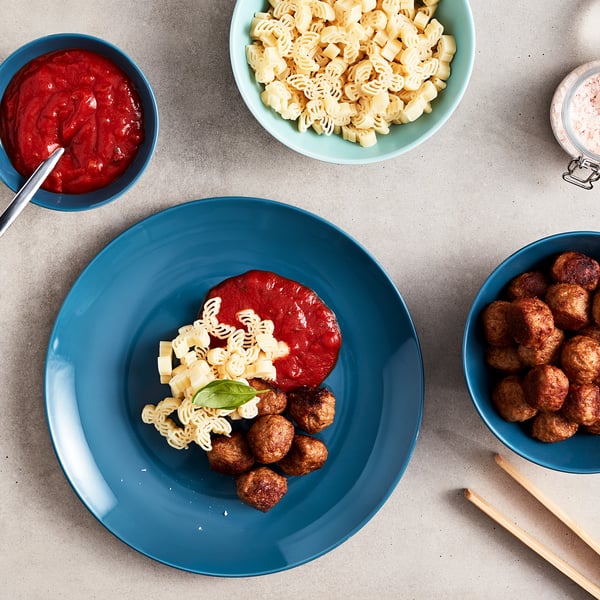 Sinine taldrik spiraalse pasta, punase kastme, lihapallidega. Kausid pasta, kastme ja lihapallidega hallil laual. Söömiseks valmis.