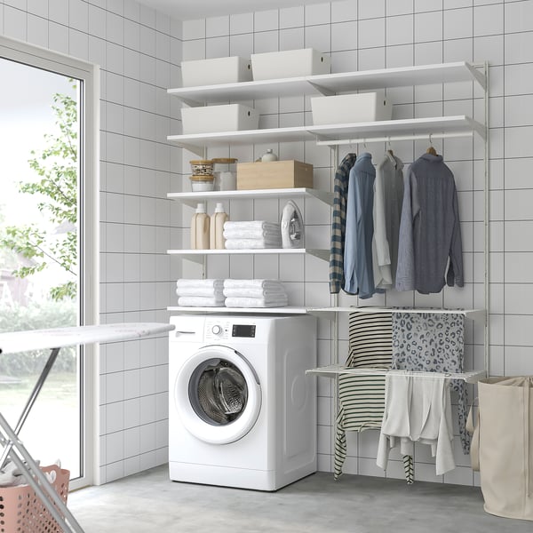 Korras pesuruum valgete BOAXEL hoiuriiulitega, kus on volditud rätikud, pudelid ja riided, valge pesumasin ja rippuvad särgid.