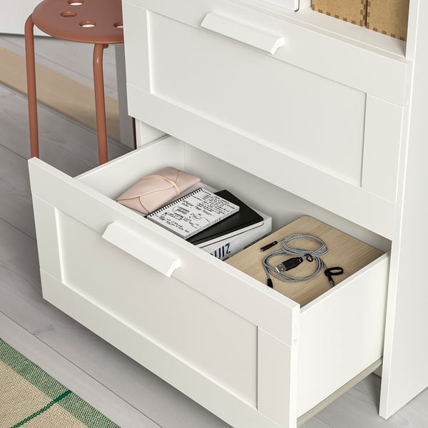 Avatud sahtliga valge telerialus, mis sisaldab raamatuid, pulti ja laadimisjuhtmeid, mis tutvustab organiseeritud hoiustamist ja kaablihaldust.