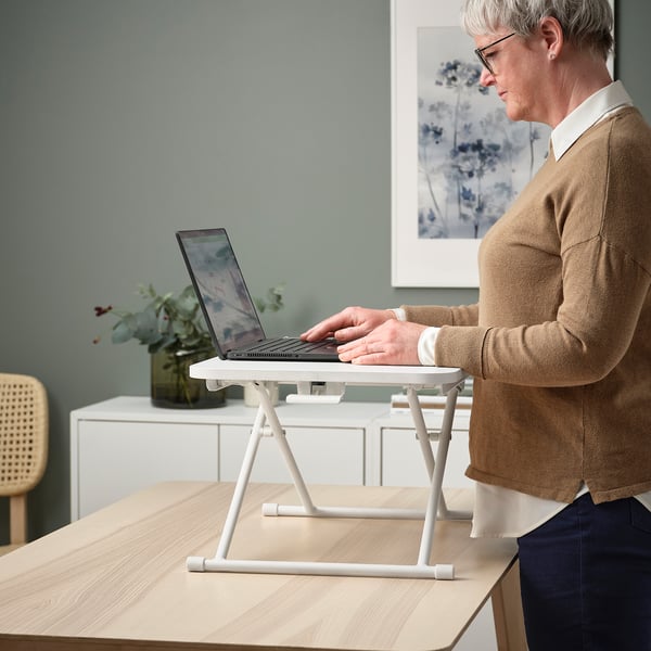 Inimene, kes kasutab ergonoomiliseks töötamiseks valget reguleeritavat sülearvutialust, vahetades istumise ja seismise vahel.