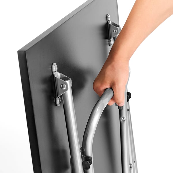 Inimene voldib käepideme abil metallist laua kokku, näidates selle kompaktset hoiustamisfunktsiooni.