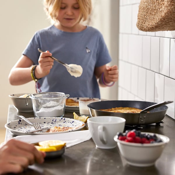 Laps küpsetab pannkooke mittenakkuval pannil, ümbritsetud koostisosade ja tööriistadega.