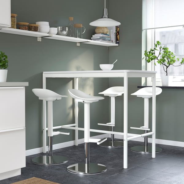 Kaasaegne minimalistlik köök nelja valge JANINGE tabureti, elegantse disaini ja metallist alustega. Hall sein, valge tööpind ja rippvalgusti.
