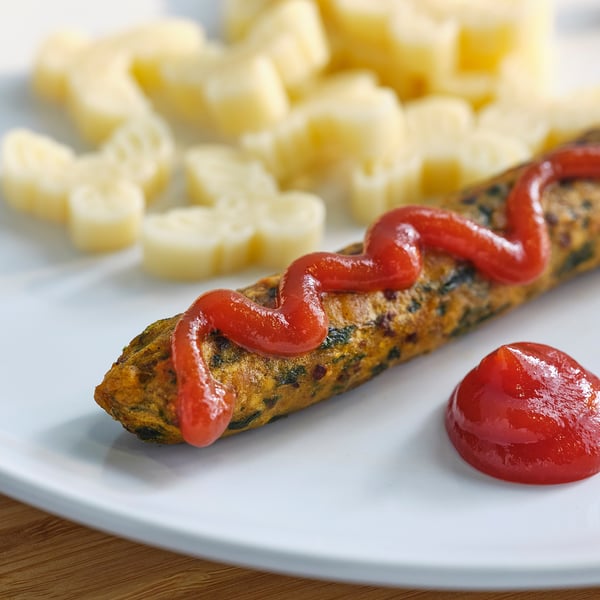 Taldrik punase ketšupiga kaetud vorsti ja ananassitükkidega.