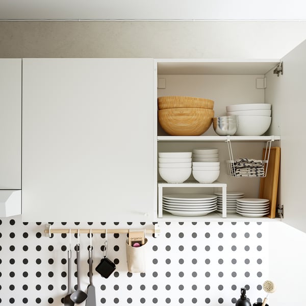 Avatud köögikapp kausside, taldrikute ja söögiriistadega. Täpiline backsplash ja rippuvad riistad.