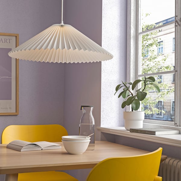 Valge lamp puidust laua kohal kollaste toolidega, taim, lillad seinad.
