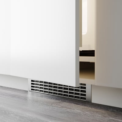 Valge kapi põhja paigaldatud väike ventilatsiooniava, tõenäoliselt ventilatsiooniks või kaablite haldamiseks kaasaegses köögis.
