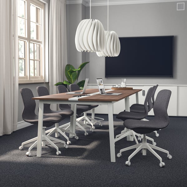 Kaasaegne konverentsiruum MITTZON laua, tumeda ülaosa, valgete jalgade, hallide toolide, suure televiisori, rippvalgusti ja laiade akendega.
