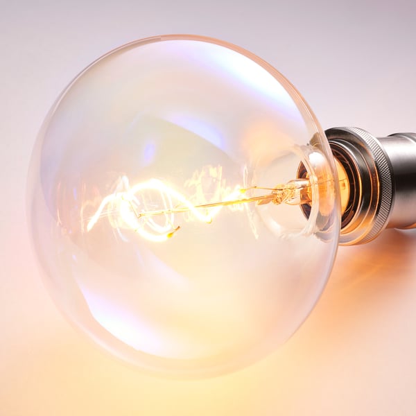 Lähivõte erksalt, hõõguvast lambipirnist, millel on spiraalhõõgniit ja topeltklaas, mis valgustab soojalt.