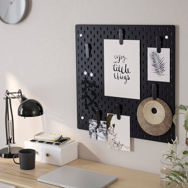 SKÅDISe perfotahvliga kirjutuslaud, kus on fotod ja märkmed; sülearvuti, lamp, kruus ja taim laual.