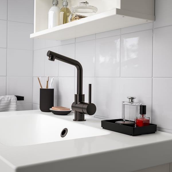Väike must SKOGSVIKEN vannitoakorraldaja istub kraanikausi kõrval, hoides käes tualetitarbeid ja meiki.