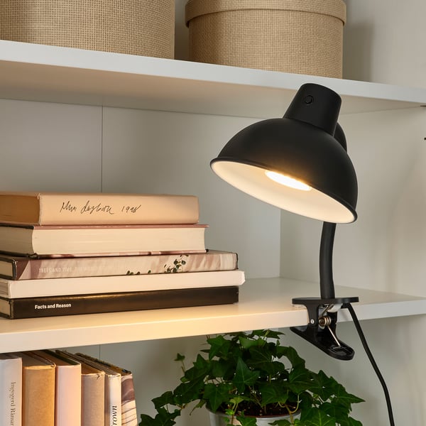 Must klambriga lamp valgustab valgel riiulil olevat raamatuvirna.