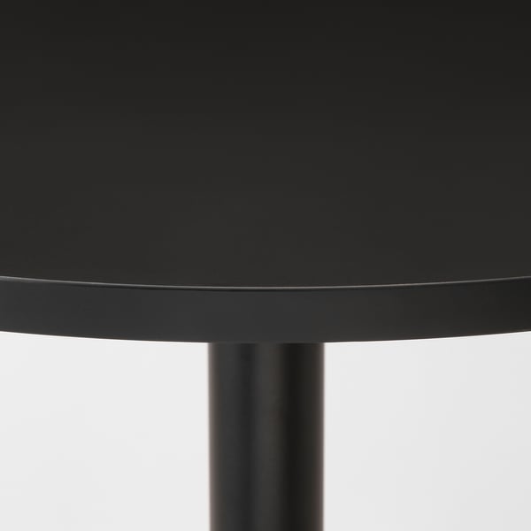 Kaasaegne must ümmargune lauaplaat, millel on klanitud serv ja silindriline jalg, istub kindlalt.