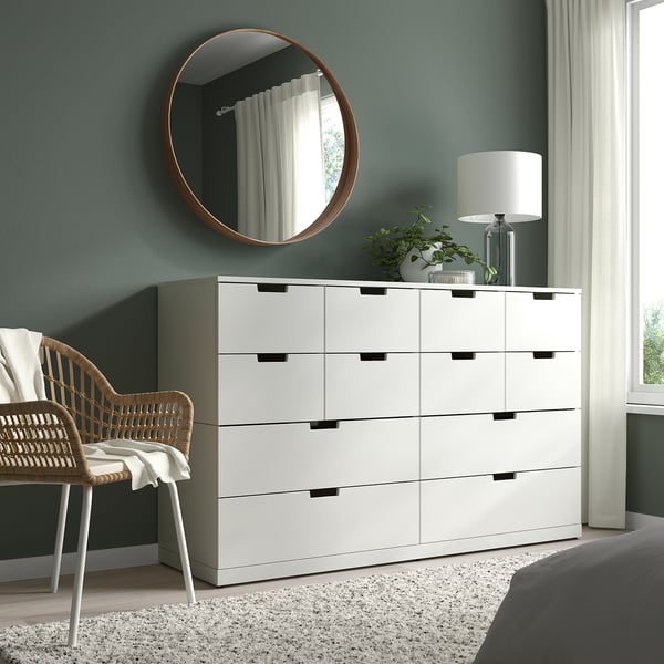 Kaasaegne magamistuba valge STOCKHOLM kummuti, peegli, vitstest tooli, lambi ja taimega.