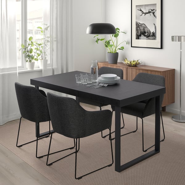 Kaasaegne söögikoht TARSELE musta laua, nelja tooli, lampide, taimega. Minimalistlik disain akna all, puidust puhvetkapi lähedal.