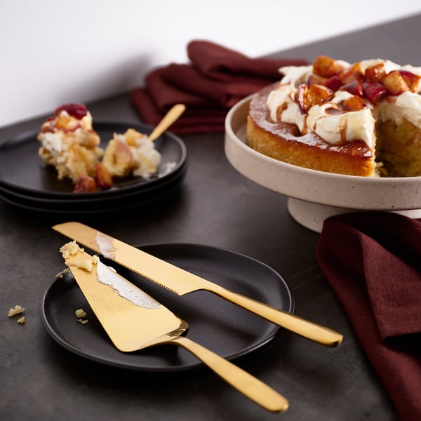 Kuldne TILLAGD koogiviil ja nuga laual, osaliselt viilutatud magustoiduga. Viiluta suureks, toetudes tumedale taldrikule, nuga pikk.