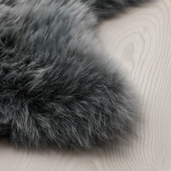 Pehme pehme lambanahast vaip, mis on laotud heledale puitpõrandale. Tekstuur näib paks ja luksuslik, kutsudes mugavust.