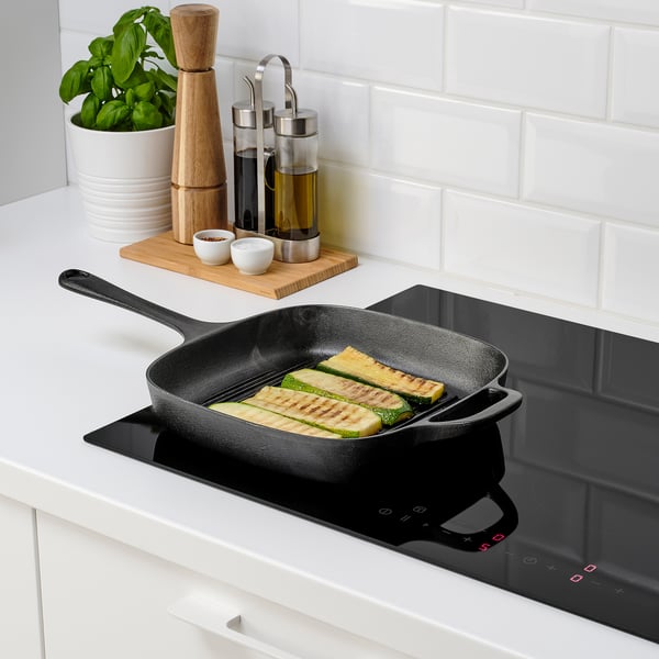 Must malmist pann pliidiplaadil grillitud suvikõrvitsaga. Ümbritsetud maitseainete ja õliga, mis näitab soojusjaotust ja vastupidavust.