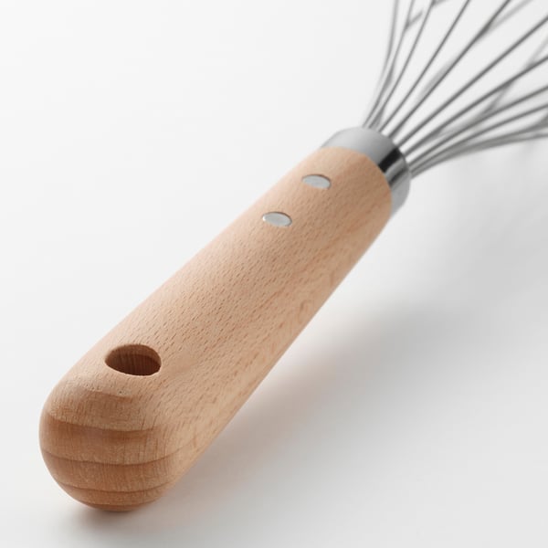 Puidust käepidemega roostevabast terasest aasadega vispel, mis on mõeldud tõhusaks segamiseks, toetudes valgele pinnale.