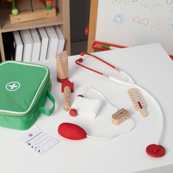 Toy medical set with stethoscope, thermometer, and syringe on table with green bag.