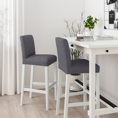 Two grey barstools with white legs and cushioned backs at a white table with plants and magazines.