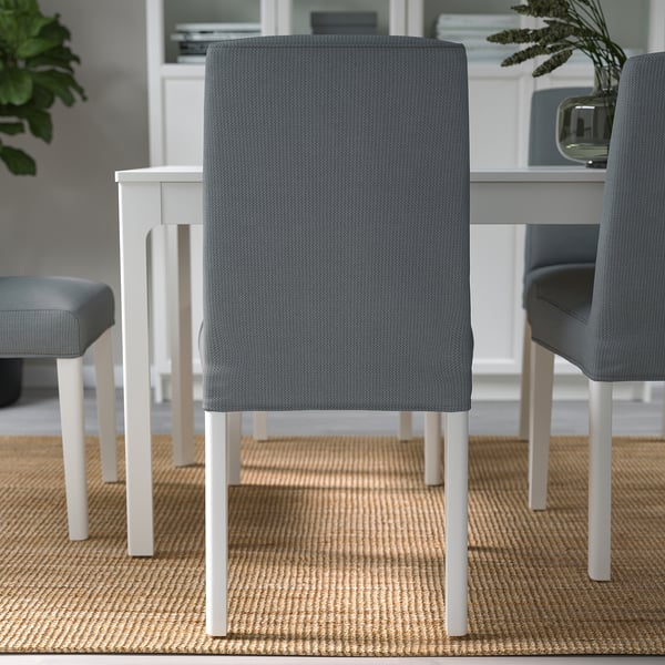 Three modern dining chairs with grey upholstery and white legs arranged around a table on a woven rug.