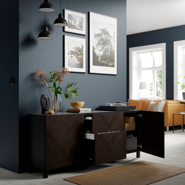 Wood sideboard with open doors revealing storage, vases, bowl on top, blue art on wall, lamps.