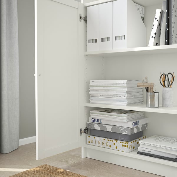 White bookcase with adjustable shelves and inset doors, storing boxes, books, and office supplies.
