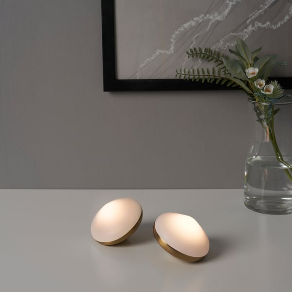 Gold BJÖRKSPIREA lamps on table with vase, soft glow.